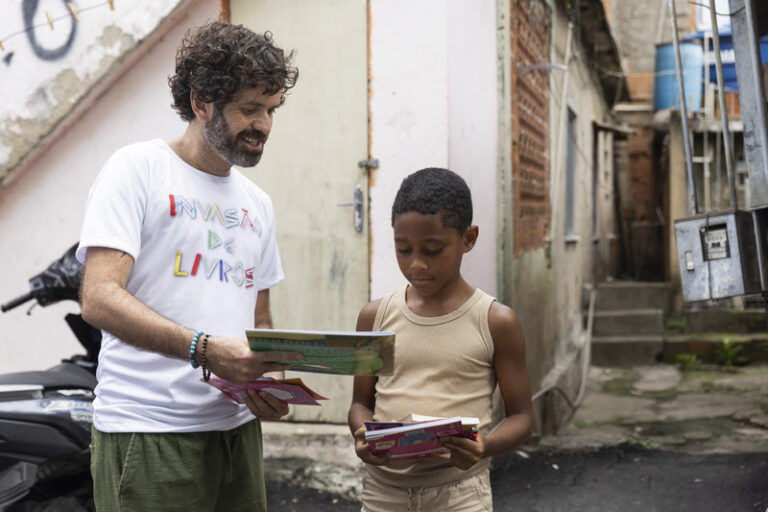 Vinicius Cortez, marketing and communications coordinator for the Rio Book Biennial, hands out a book to a child at Complexo da Alemão